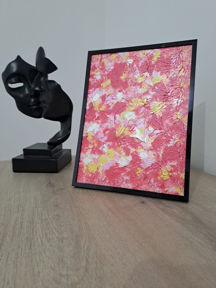 "Feu de pétales rouges" Un cadre avec une œuvre colorée sur une table et une sculpture noire à côté.