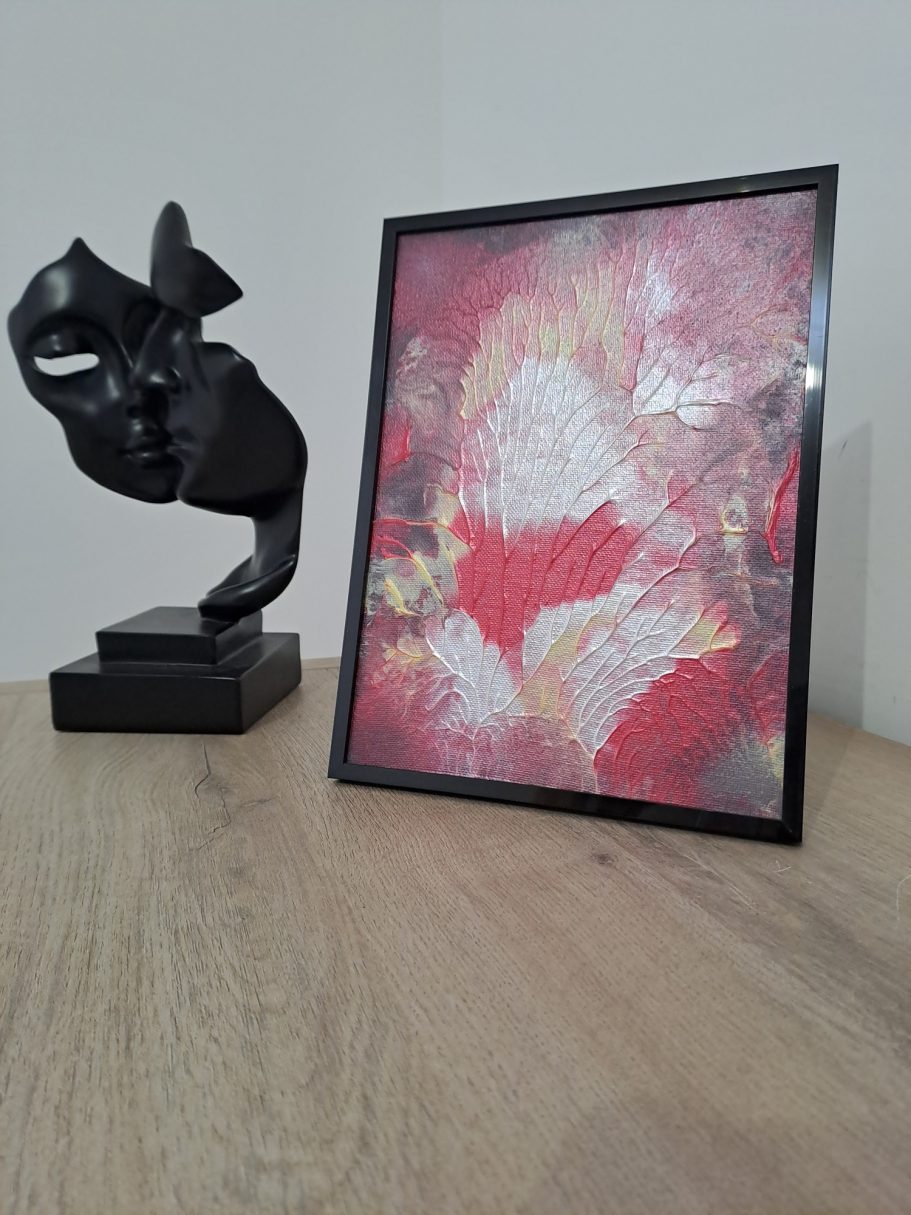 "Souffle de braise" Table en bois avec une sculpture noire et un cadre contenant une œuvre artistique colorée.